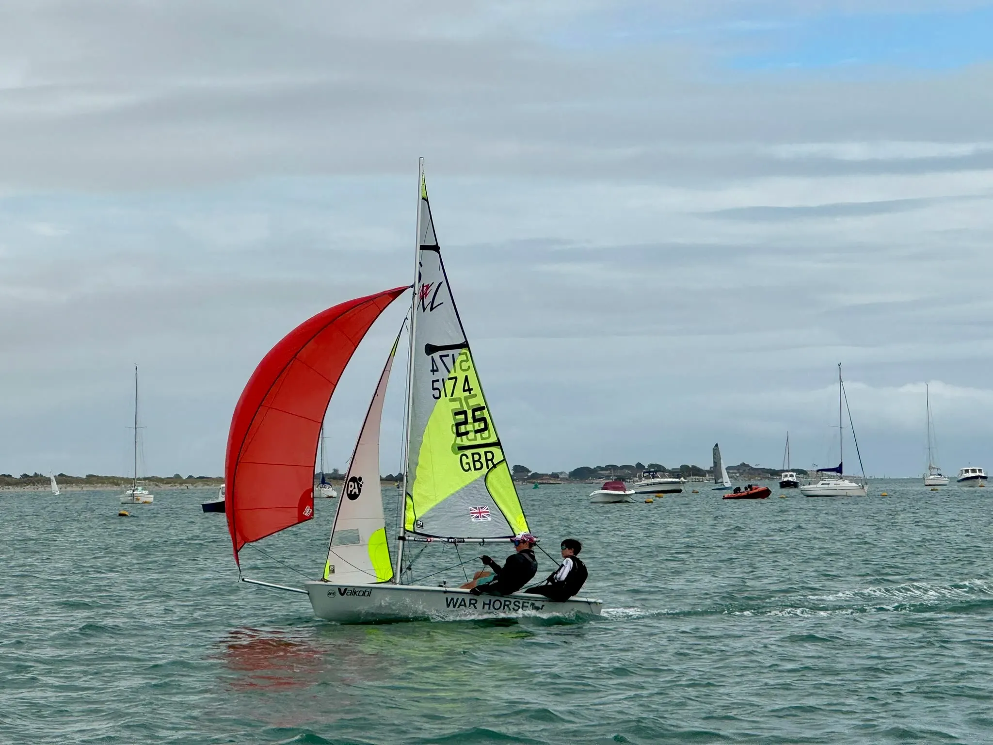 Two sailors flying a red spinnaker on an RS Feva